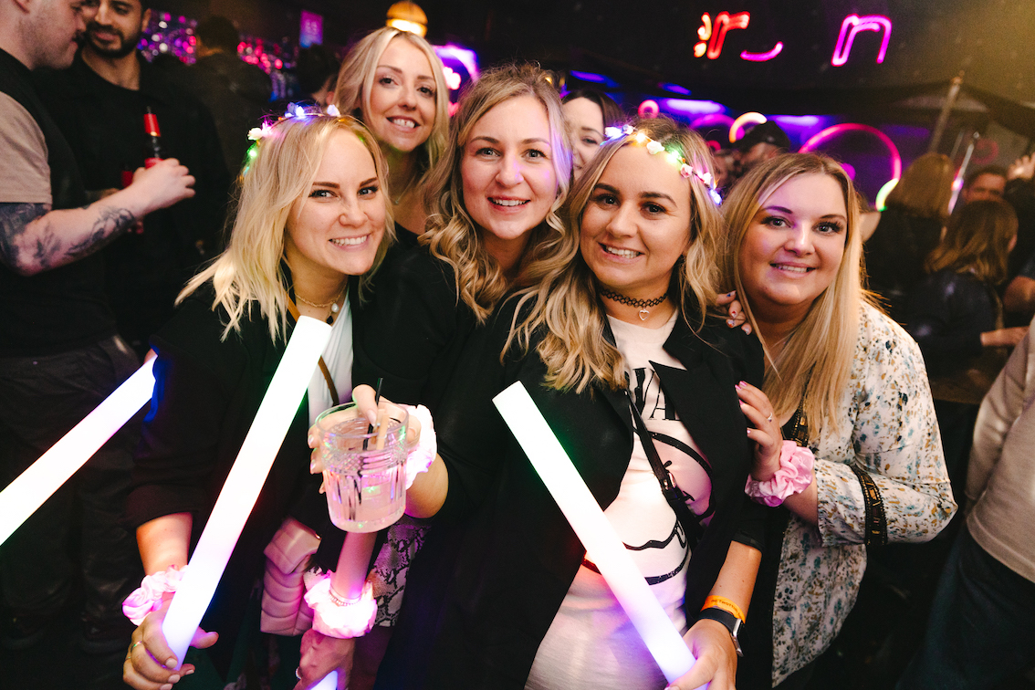 5 women on a hen do wearing sashes and drinking cocktails