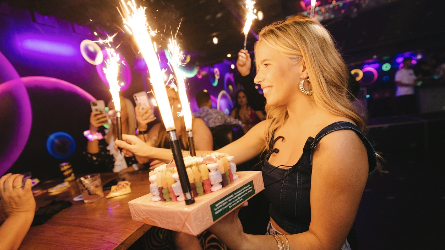 woman smiling in glowing ball pit and throwing plastic balls into the air